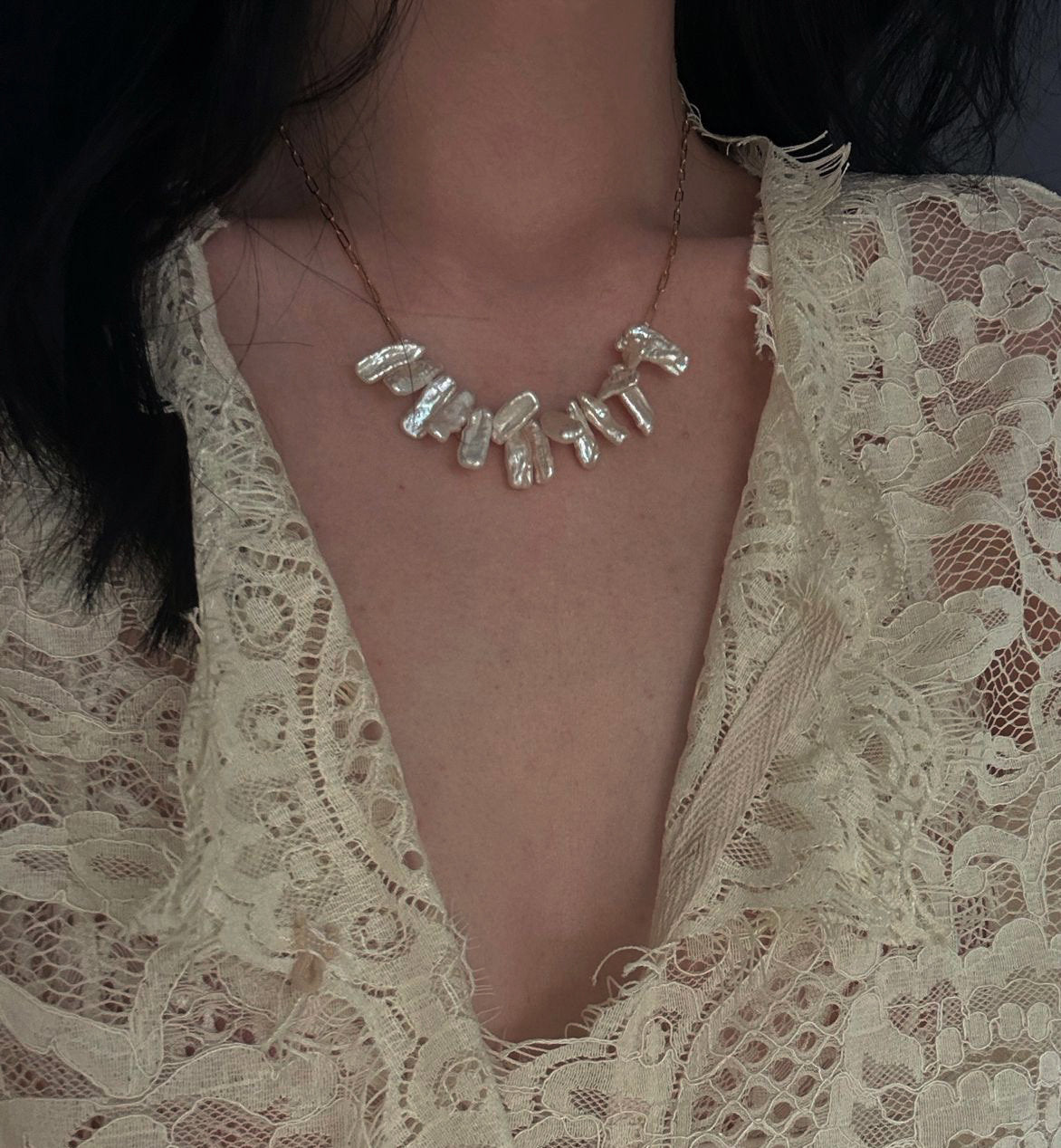 Freshwater pearl necklace worn around the collarbone with a delicate gold chain