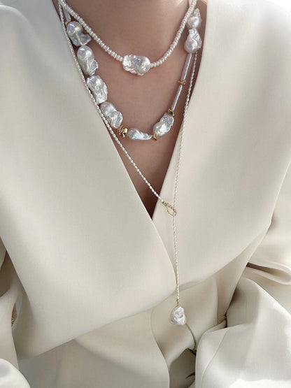 Keshi pearl lariat necklace displayed over brown leather and stone props.