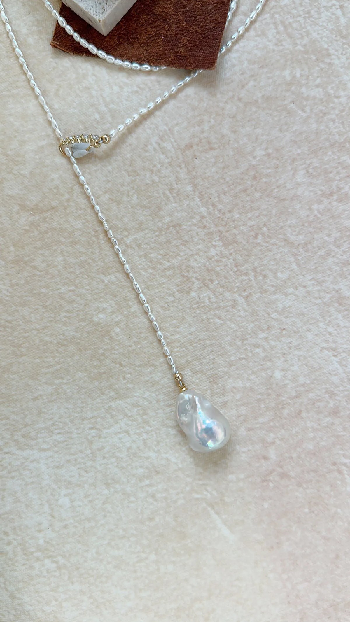 Flatlay of the Keshi pearl Y-lariat necklace with gold CZ slider clasp on neutral fabric.