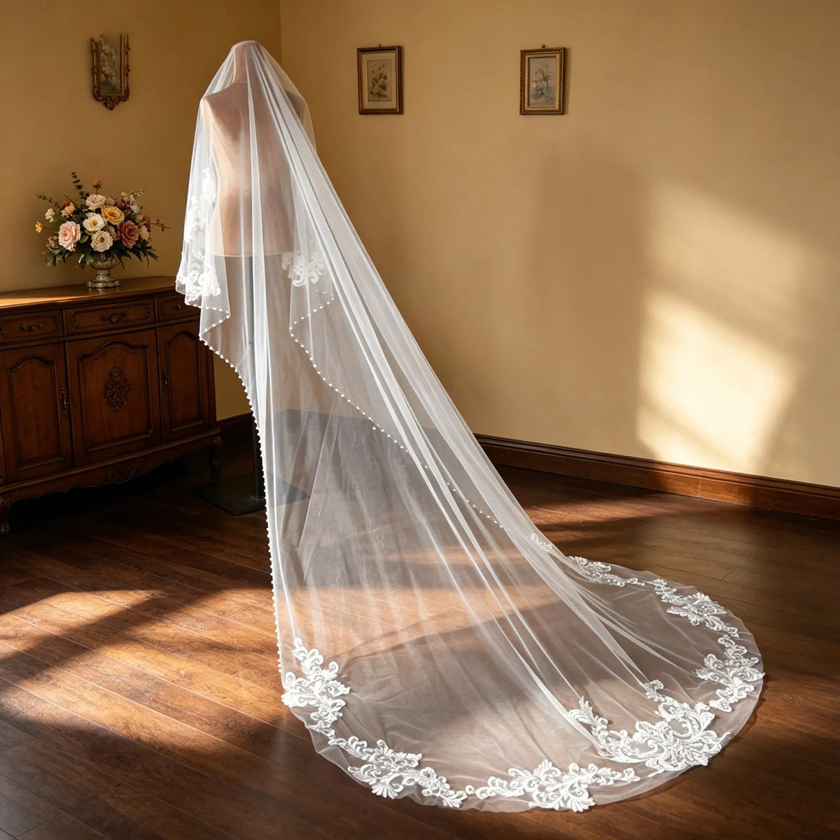 Side angle of studio mannequin displaying long drape of lace appliqué cathedral veil on hardwood floor
