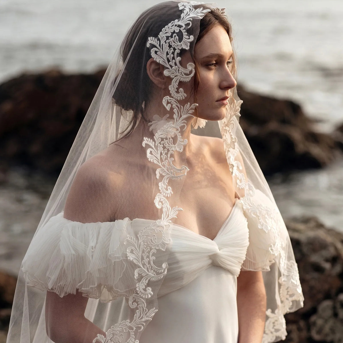 Outdoor close-up portrait of bride wearing sheer veil draped over face with lace embroidery trim