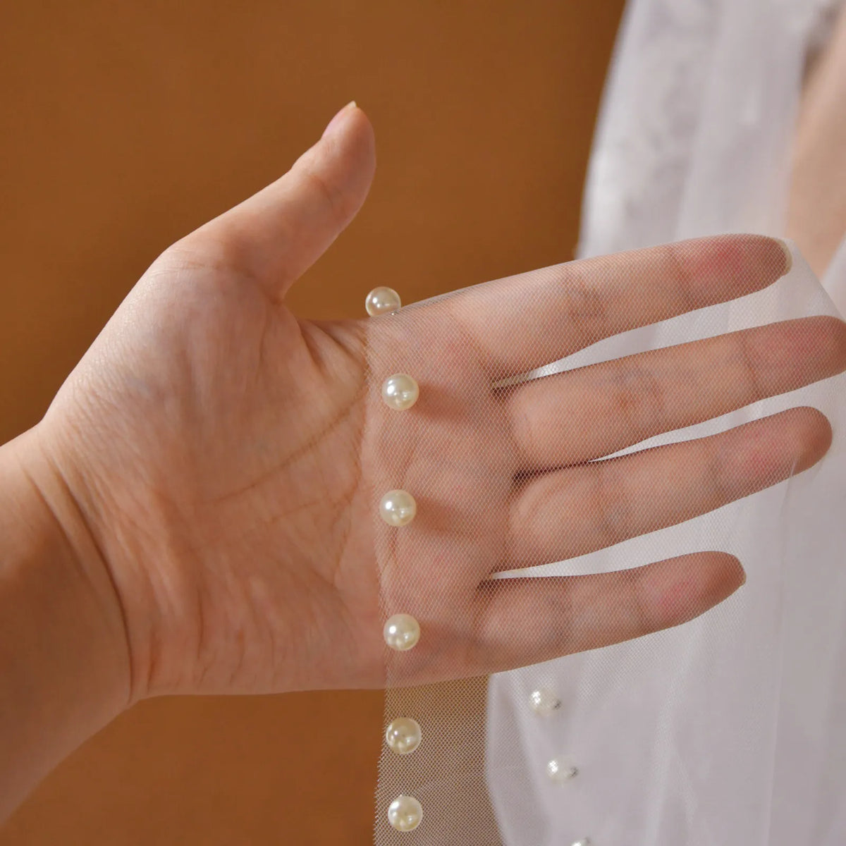 Close-up hand shot showcasing line of attached faux pearls along delicate tulle mesh edge