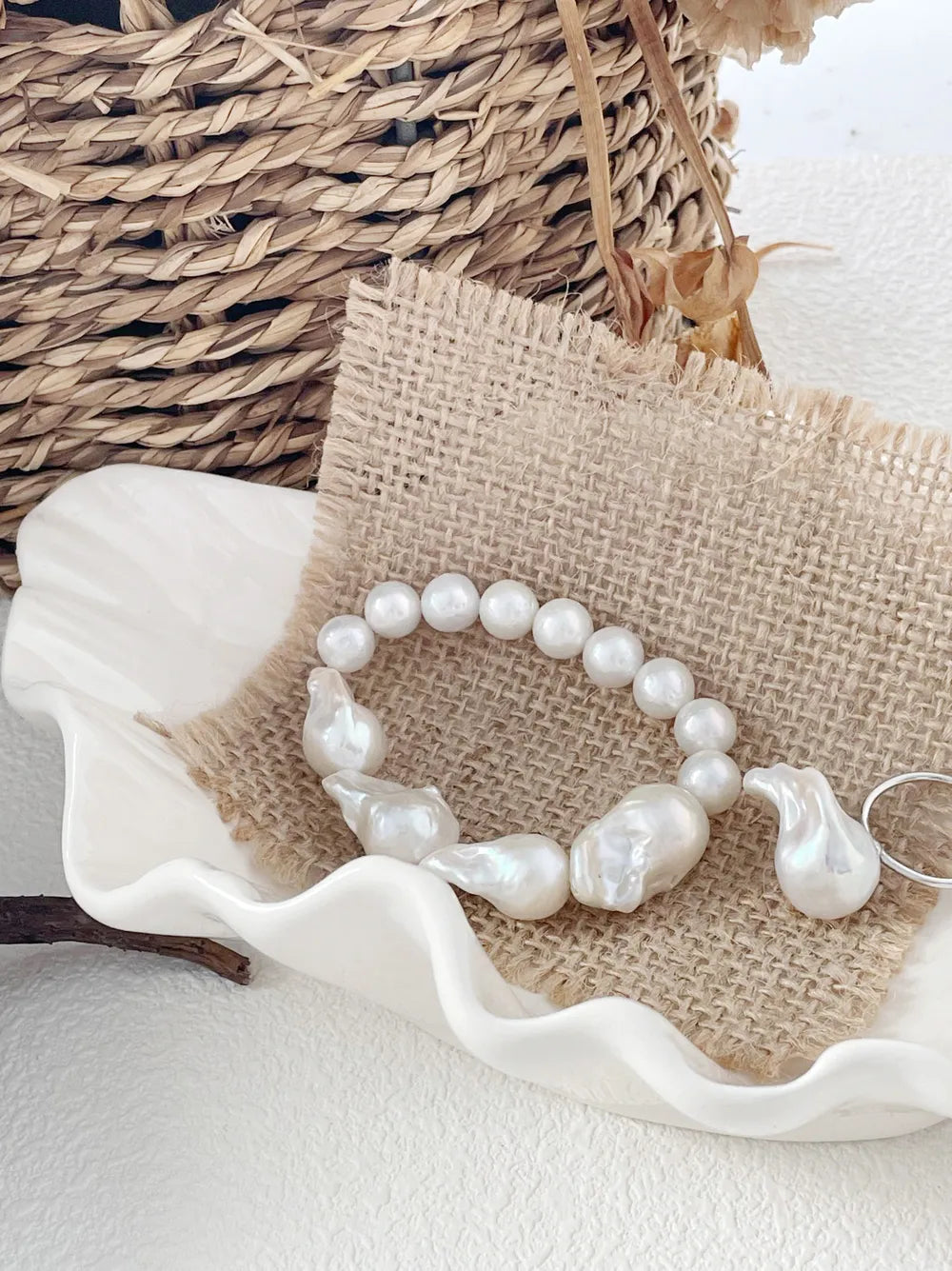 Large baroque pearl and round pearl spliced elastic bracelet displayed on burlap and shell dish.
