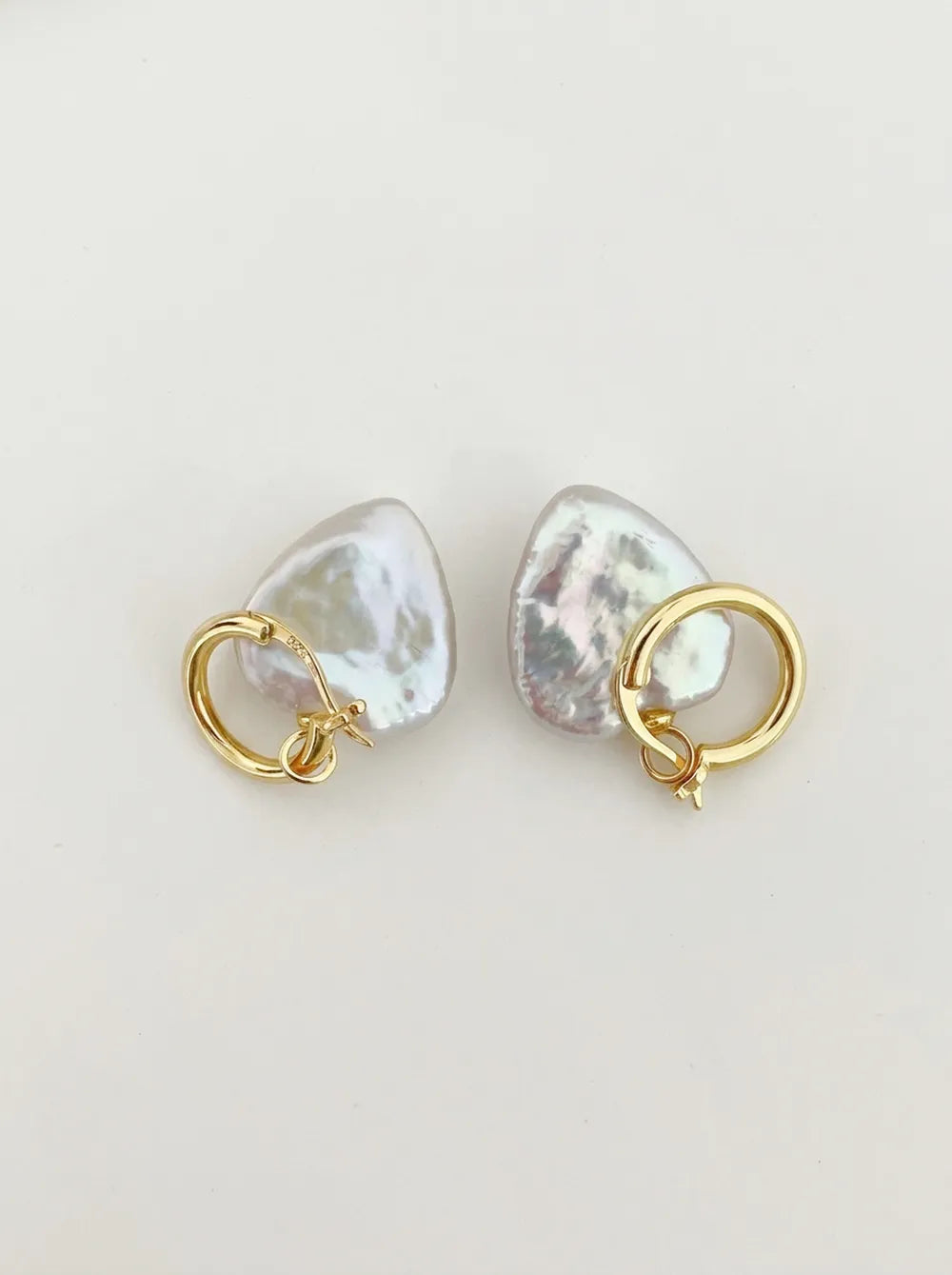 Pair of large heart baroque pearl huggie hoop earrings with 18k gold plated clasp flatlay on white background.