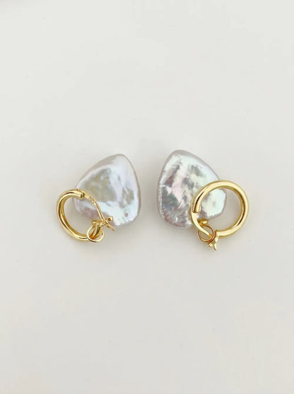 Pair of large heart baroque pearl huggie hoop earrings with 18k gold plated clasp flatlay on white background.