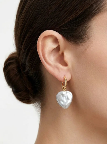 Model with hair in a bun wearing the large heart-shaped baroque pearl huggie earring.