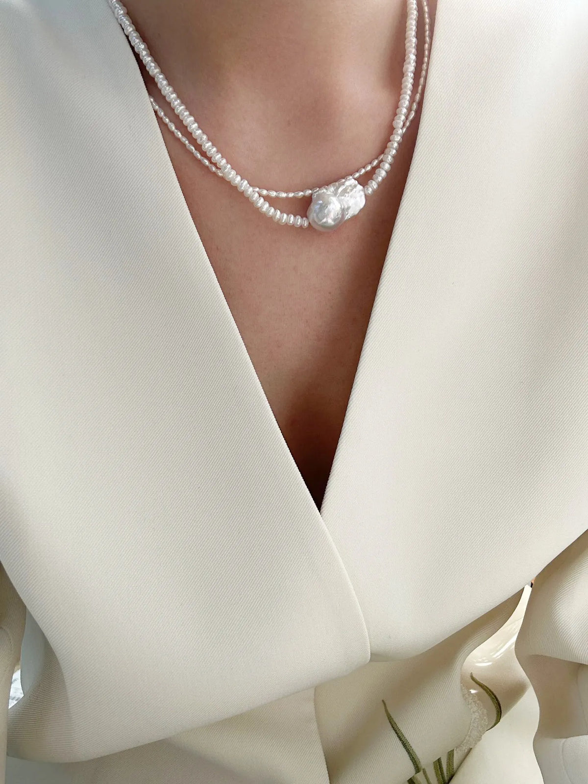 Model styling layered baroque pearl choker necklaces with a modern white suit