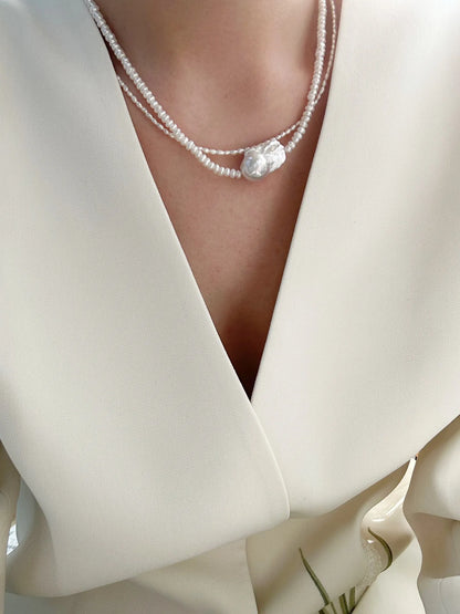 Model styling layered baroque pearl choker necklaces with a modern white suit