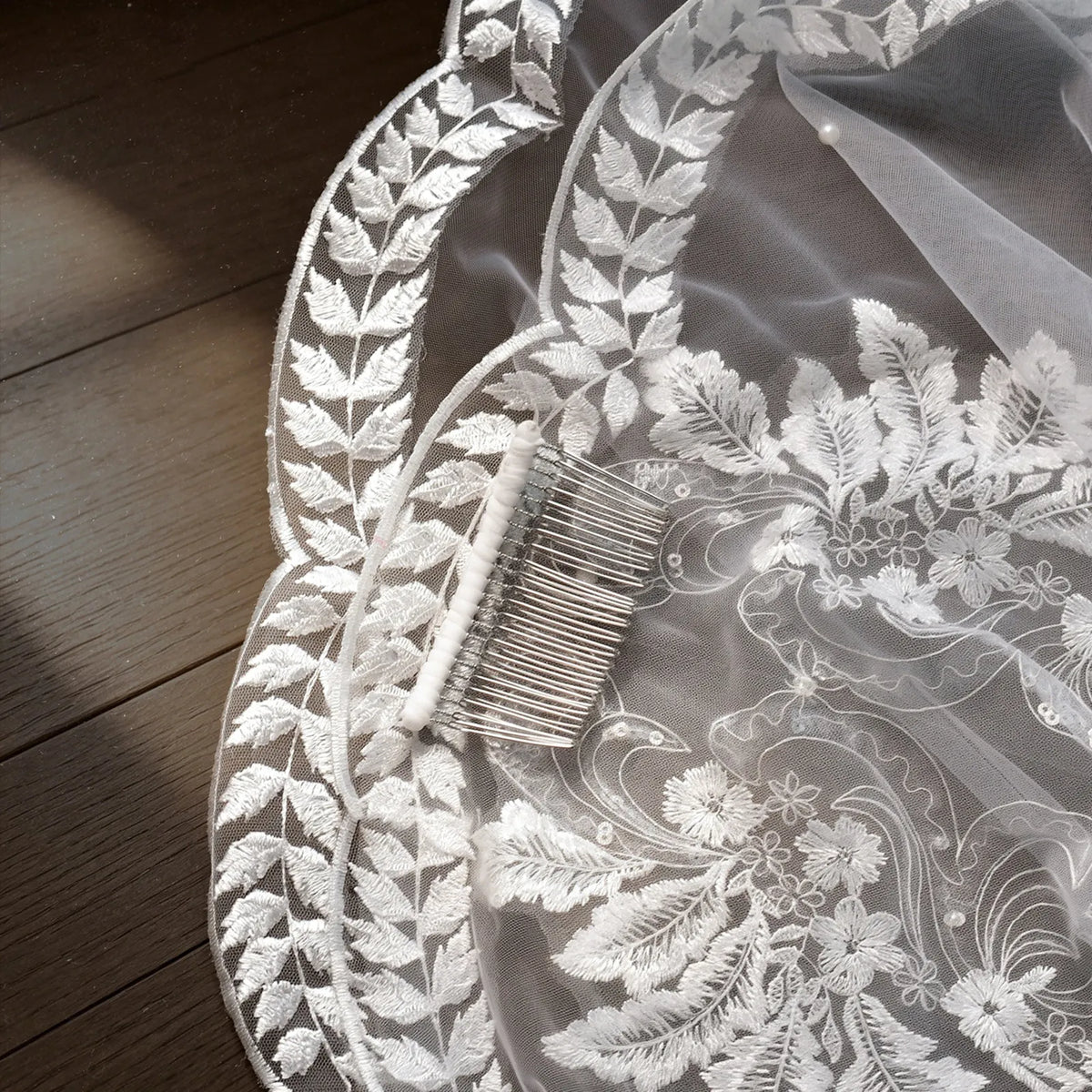 Close up of metal comb attached to cathedral veil featuring leafy embroidered lace trim and scatter pearls
