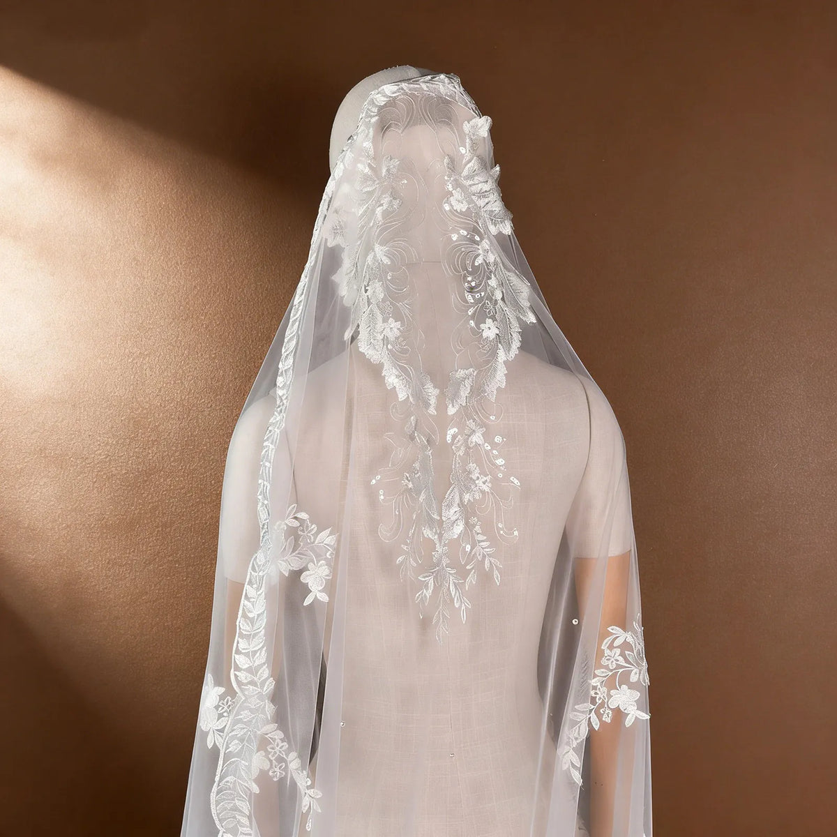 Back view of mannequin wearing chapel veil with intricate embroidered floral lace cap and scattered pearl embellishments