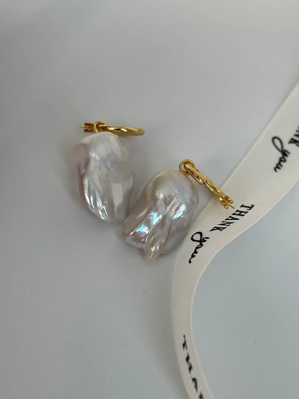 Lustrous flame baroque pearl hoop earrings displayed beside a ribbon prop.