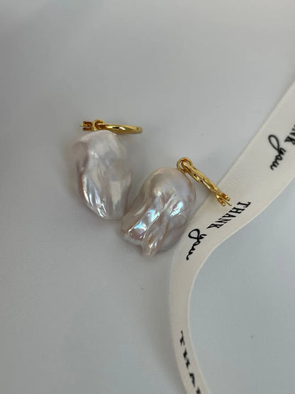 Lustrous flame baroque pearl hoop earrings displayed beside a ribbon prop.