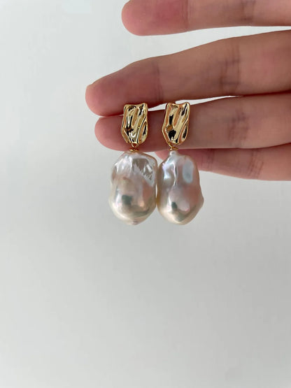 Close-up of open hand holding the large baroque pearl drop earrings with intense rainbow luster.