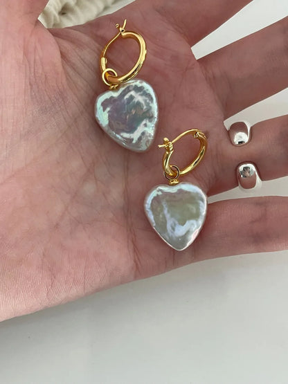 Open palm holding the large heart-shaped baroque pearl earrings showcasing intense nacre luster.