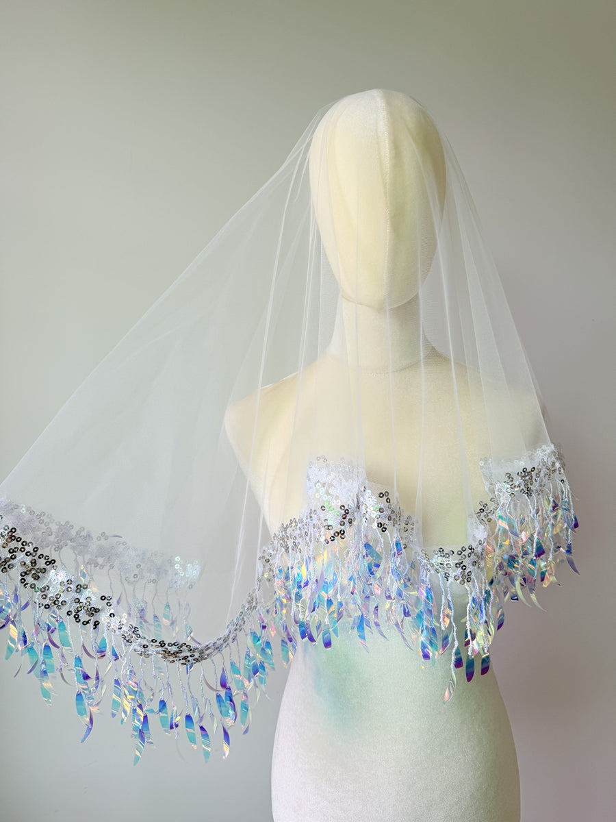 Whimsical mermaidcore style single-tier drop bridal veil featuring sheer white tulle hemmed with iridescent holographic leaf sequin tassels.
