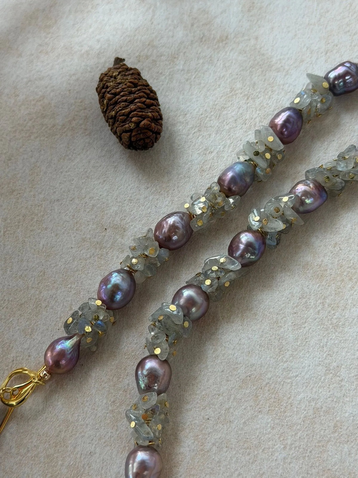 Macro shot highlighting iridescent luster of purple baroque pearls and moonstone chips with gold accents.