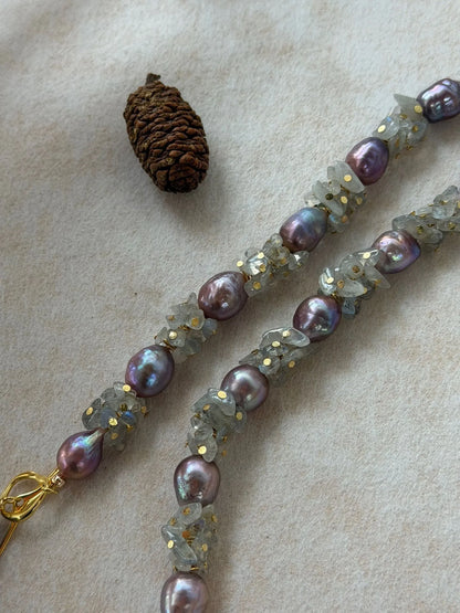 Macro shot highlighting iridescent luster of purple baroque pearls and moonstone chips with gold accents.