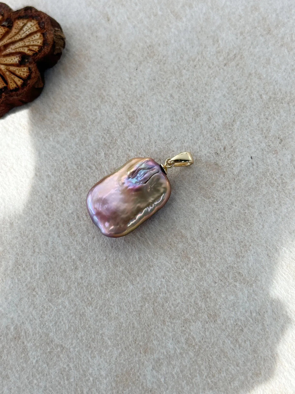 Close-up view of metallic purple square baroque pearl pendant on soft felt background.
