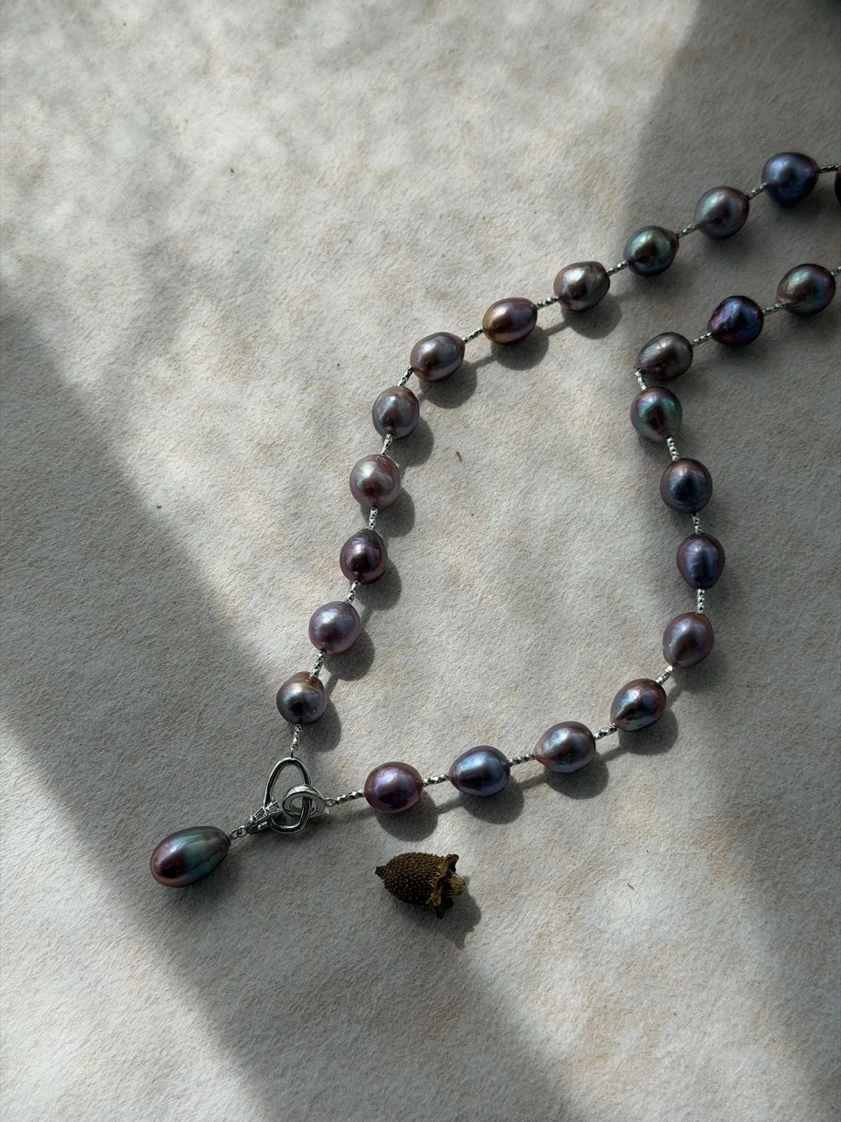 Metallic violet baroque pearl Y-necklace showing deep iridescent luster under bright sunlight.