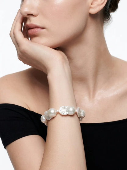 Model holding hand to chin displaying the rice and large baroque pearl strand bracelet on wrist.