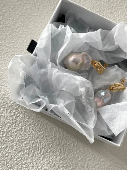 Molten metal baroque pearl earrings displayed inside a white tissue-lined jewelry gift box.