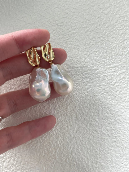 Hand holding the molten metal gold S925 silver baroque pearl earrings demonstrating scale and luster.