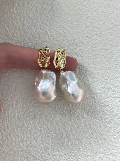 Pair of molten gold metal stud baroque pearl earrings held over a finger showing post detail.