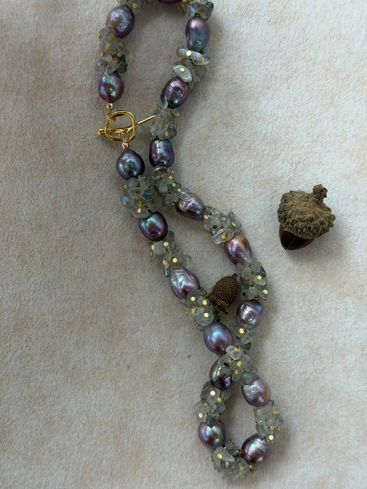 Twisted display of moonstone chips and metallic purple baroque pearls on soft background.