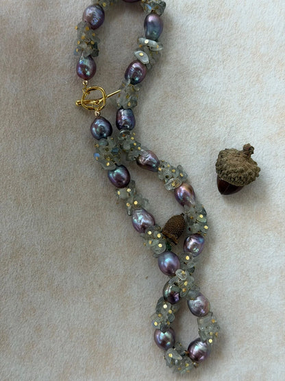 Twisted display of moonstone chips and metallic purple baroque pearls on soft background.