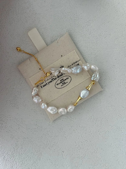 Moustache baroque pearl bracelet resting on a beige printed linen jewelry pouch.