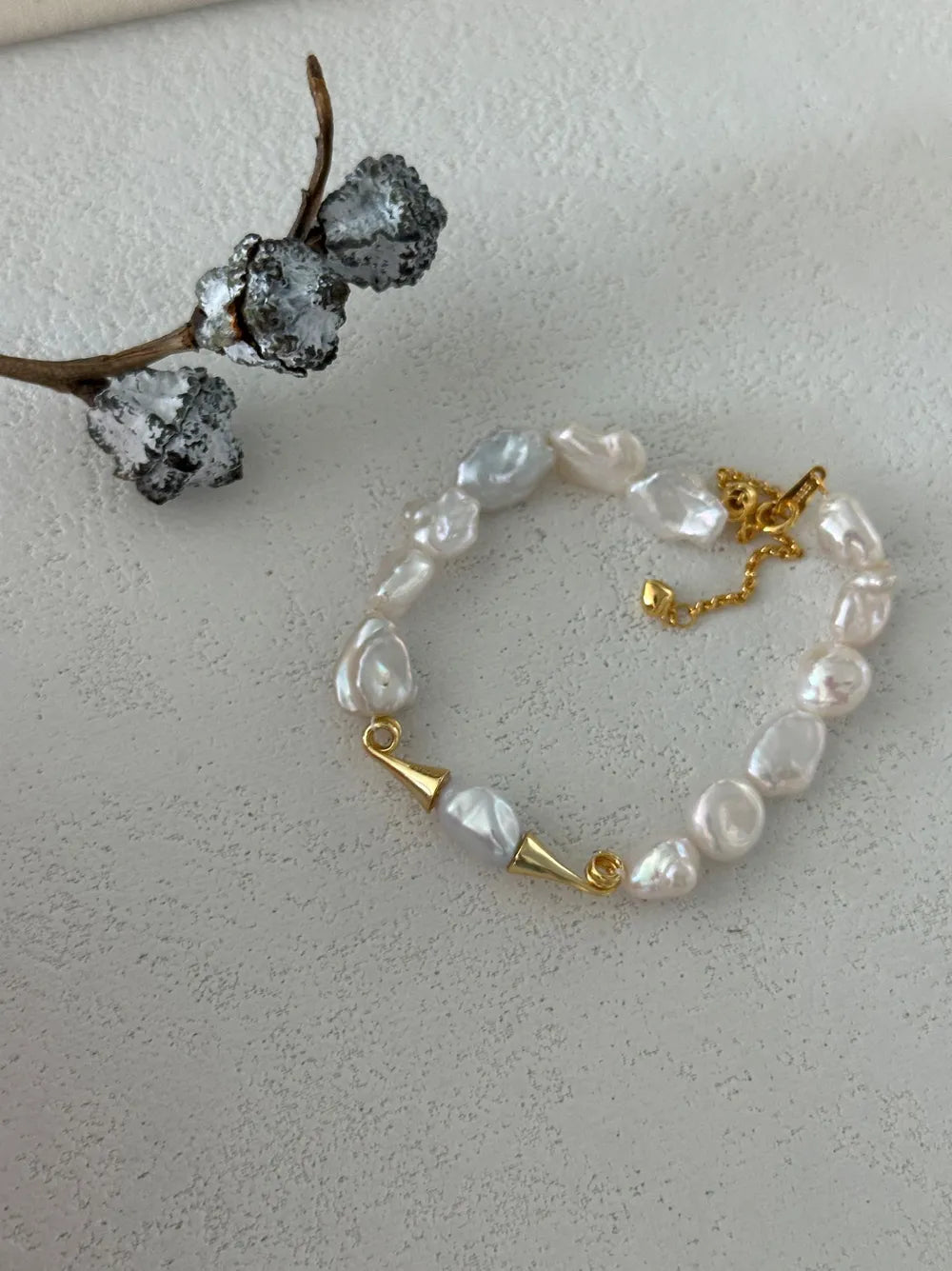 Moustache baroque pearl bracelet displayed next to a cotton pod prop on white background.