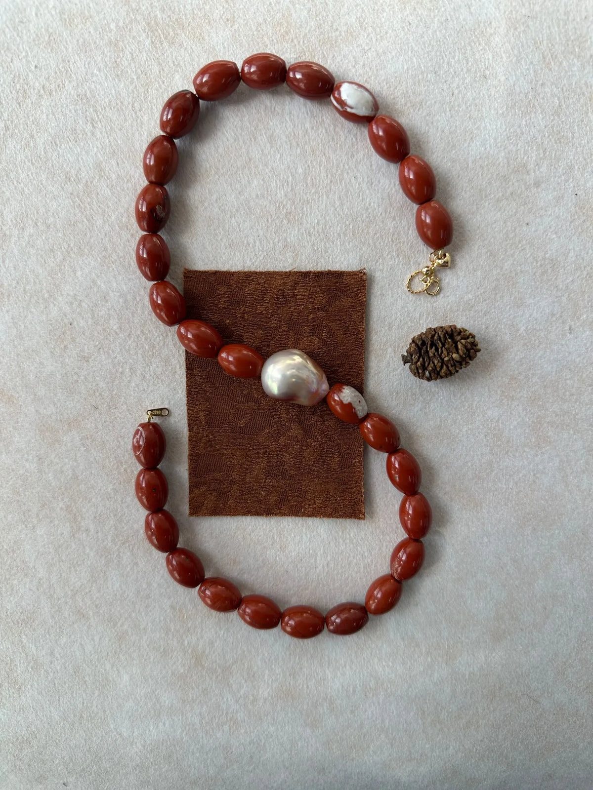 S-shape flatlay display of natural red jasper beaded necklace with center baroque pearl.