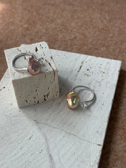 Top view of a pair of bean baroque pearl solitaire cz open rings on white travertine stone.