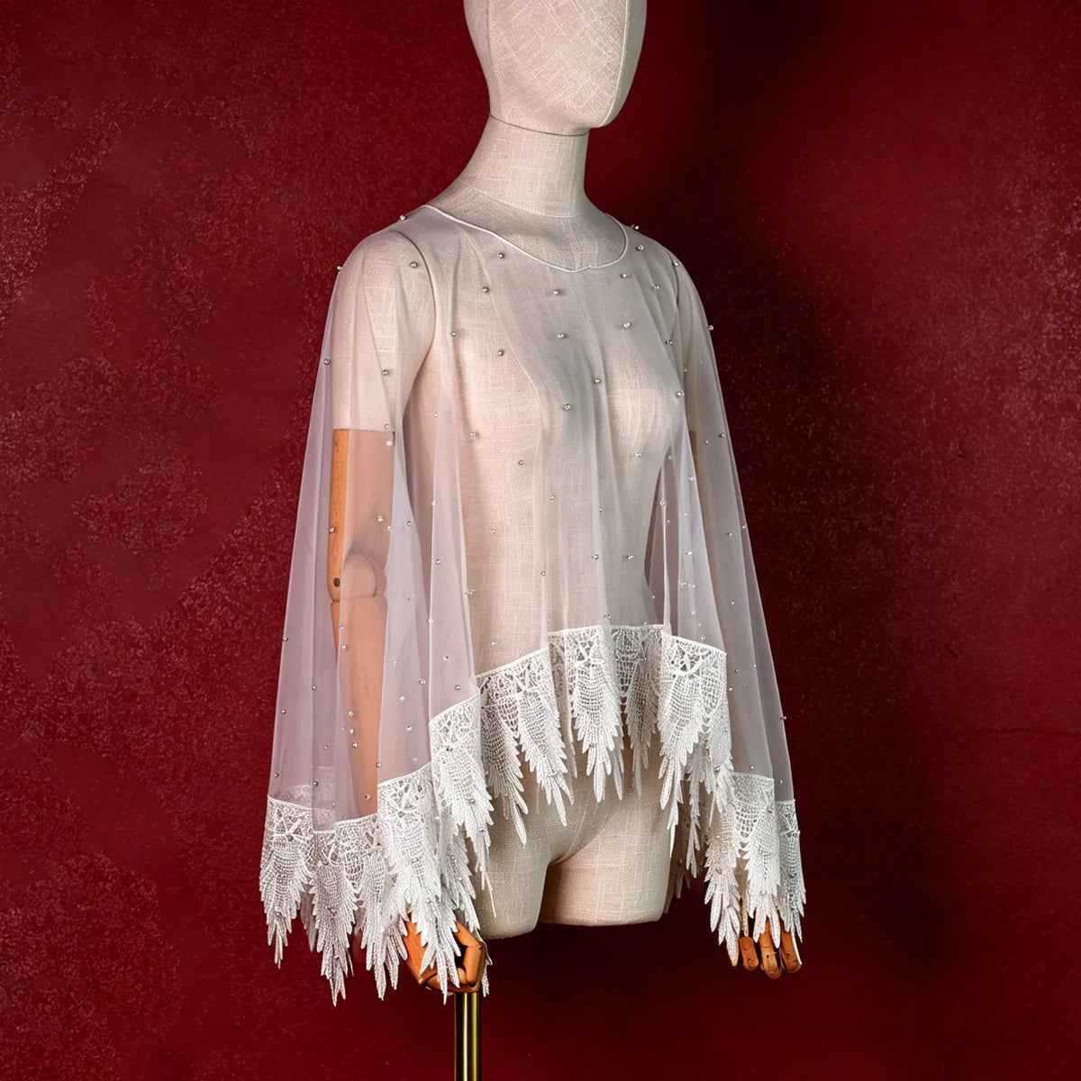 Side view of mannequin displaying ivory pearl studded tulle capelet with pointed crochet lace border