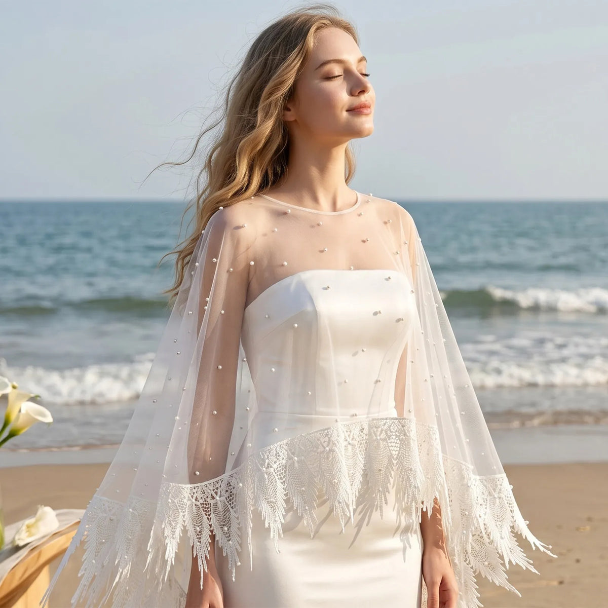 Bride with closed eyes wearing sheer pearl capelet on sunny beach with ocean background