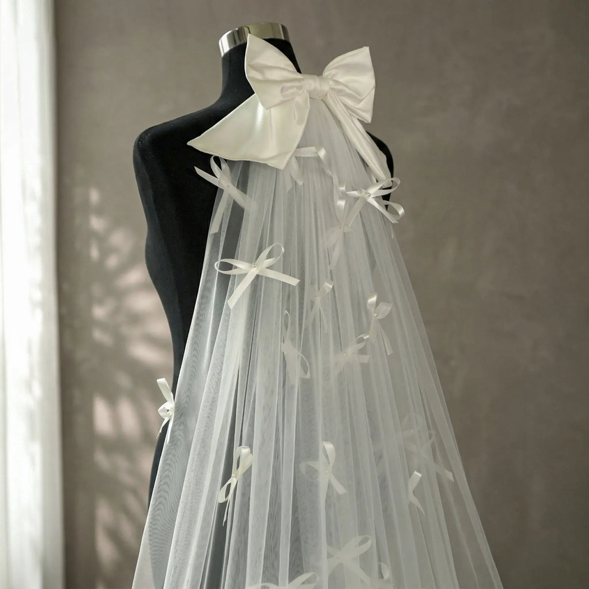 Bride standing in indoor studio next to floral vase showing full circular drape of pearl bow veil