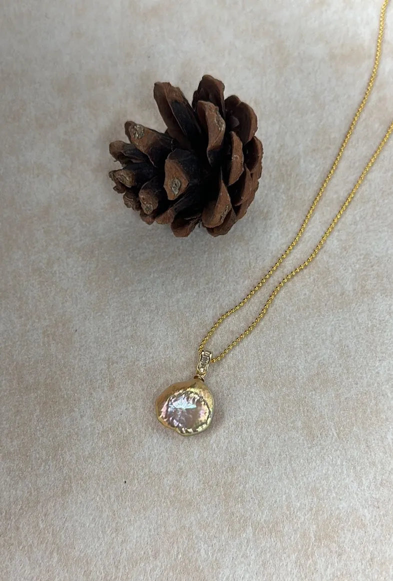 Petal baroque pearl pendant on metallic beaded chain against light background