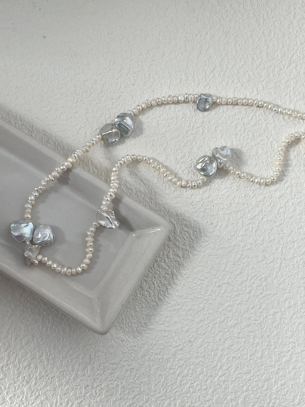 Close-up of petal-shaped freshwater pearl necklace displayed on a sleek ceramic tray