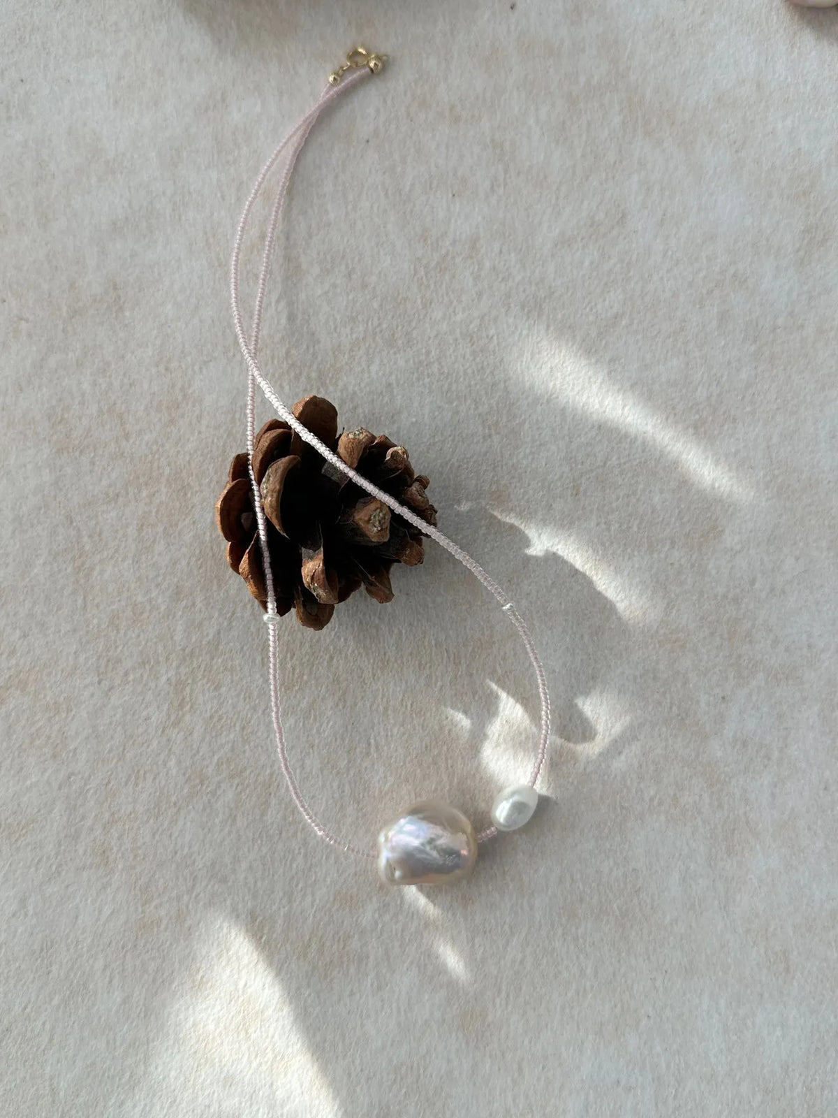 Pink baroque pearl choker with micro-bead strand in natural sunlight with pinecone prop.