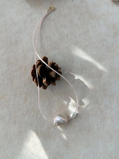 Pink baroque pearl choker with micro-bead strand in natural sunlight with pinecone prop.