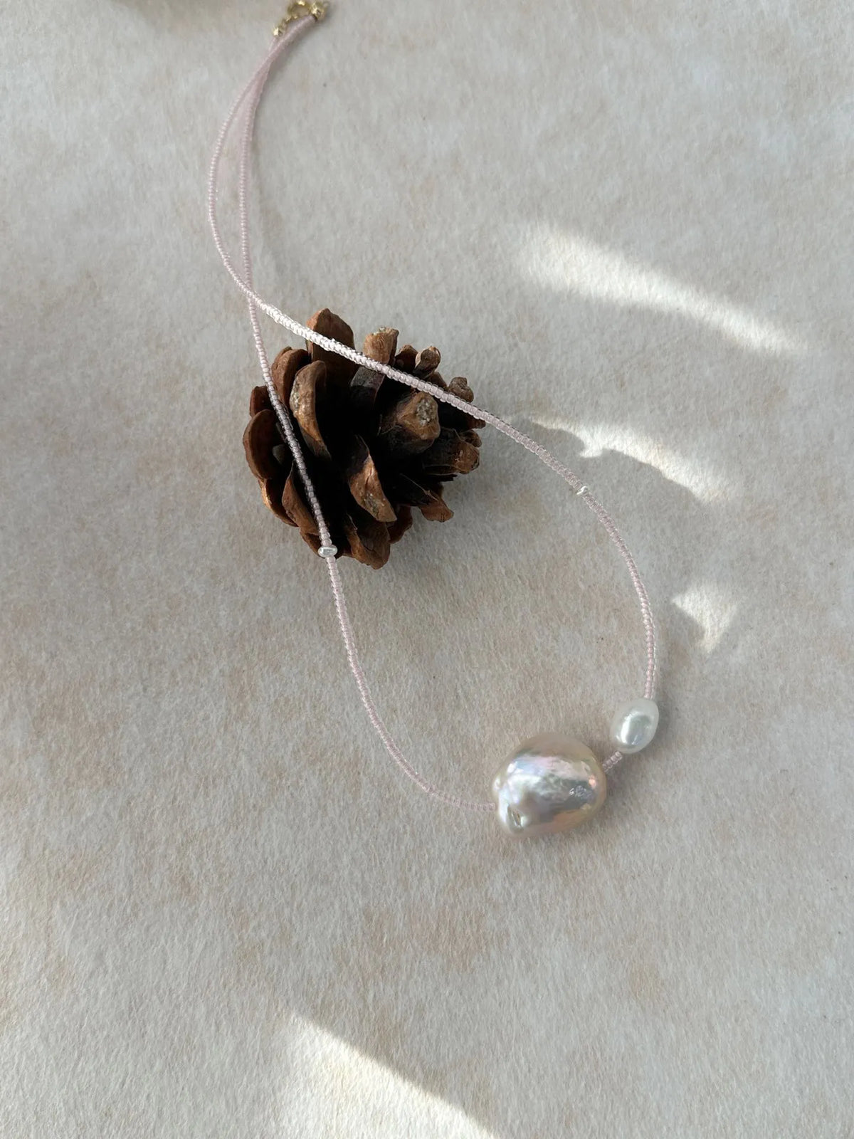 Close-up of pink baroque pearl duo on pink beaded chain displayed with pinecone prop.