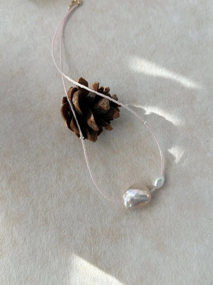 Close-up of pink baroque pearl duo on pink beaded chain displayed with pinecone prop.