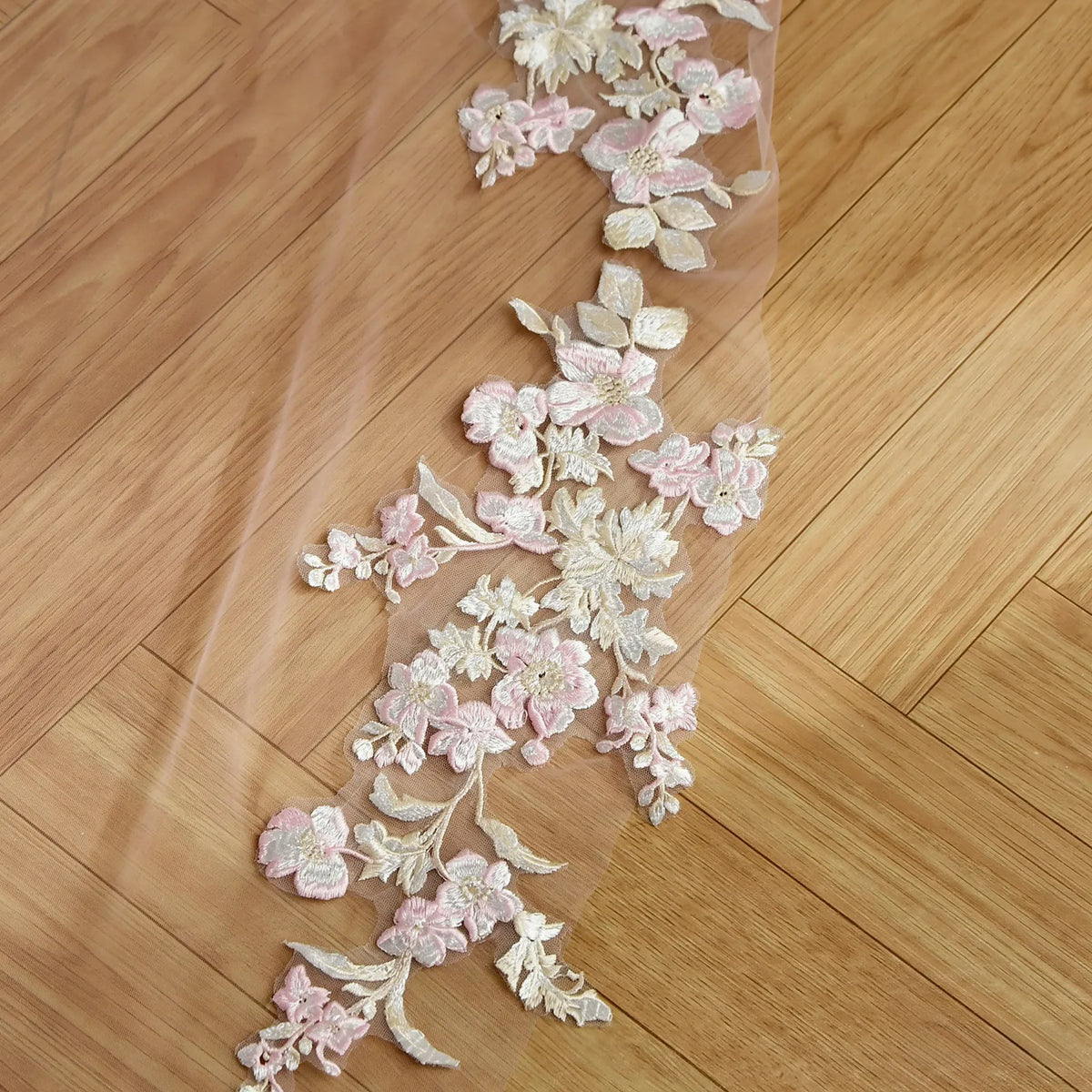 Close-up flatlay of pink and ivory floral leaf embroidery appliqué on sheer soft pink mesh