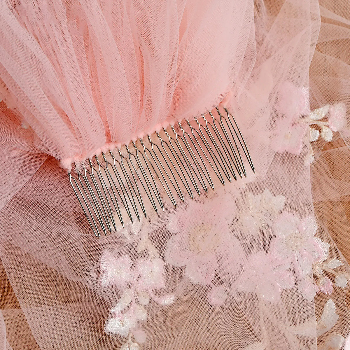 Close-up of sturdy metal hair comb stitched onto soft pink gathered tulle mesh