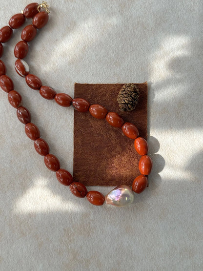 Close-up of red jasper necklace draped over brown fabric prop with pinecone accent.