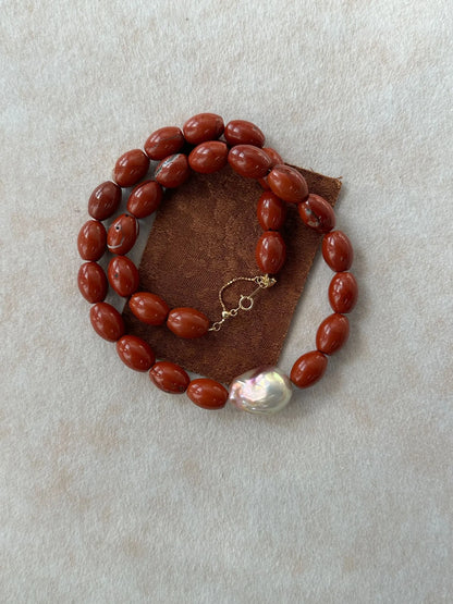 Coiled display of red jasper and baroque pearl necklace on brown felt fabric.