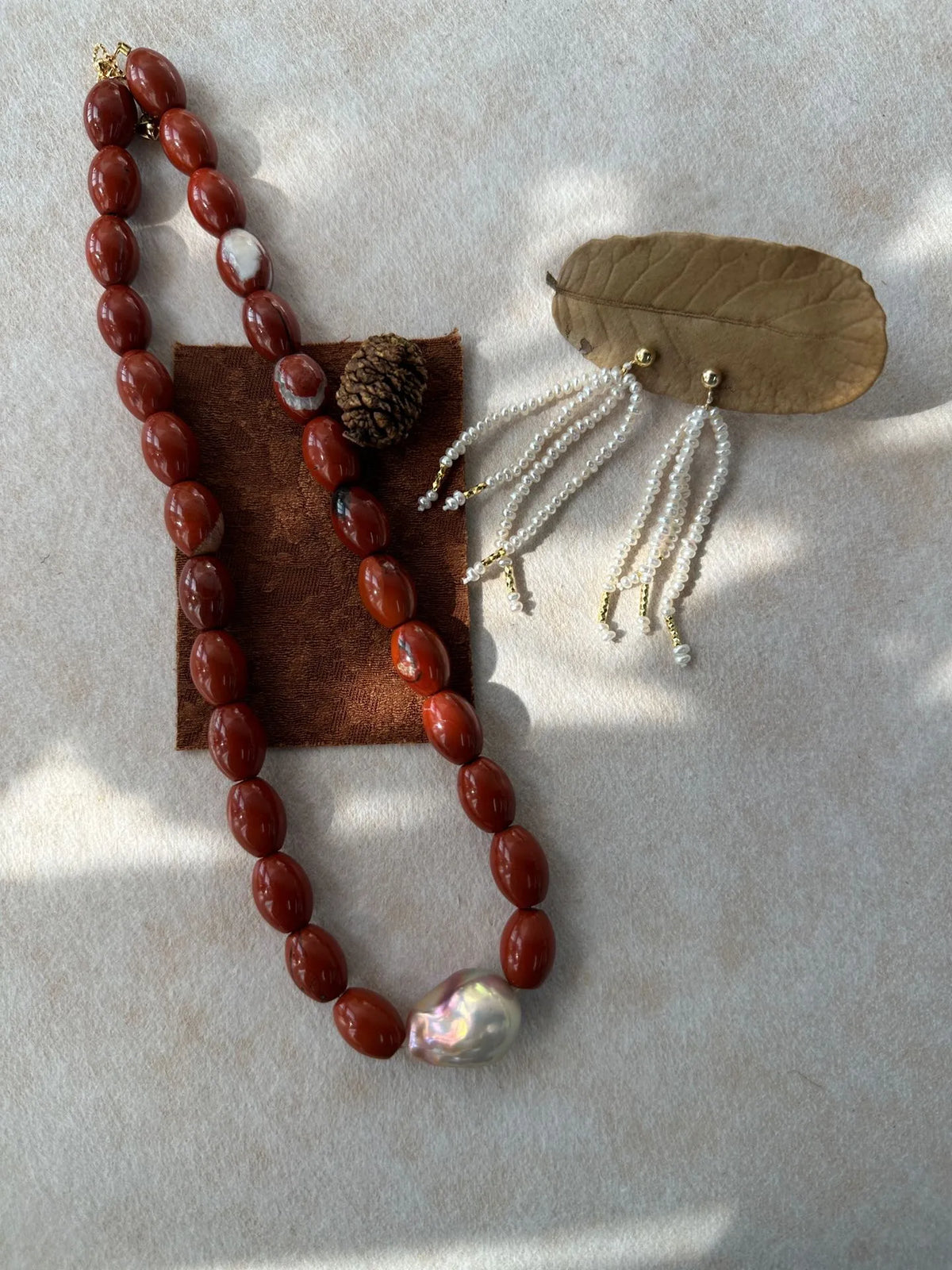 Red jasper baroque pearl necklace flatlay styled with pearl tassel earrings and dry leaf prop.