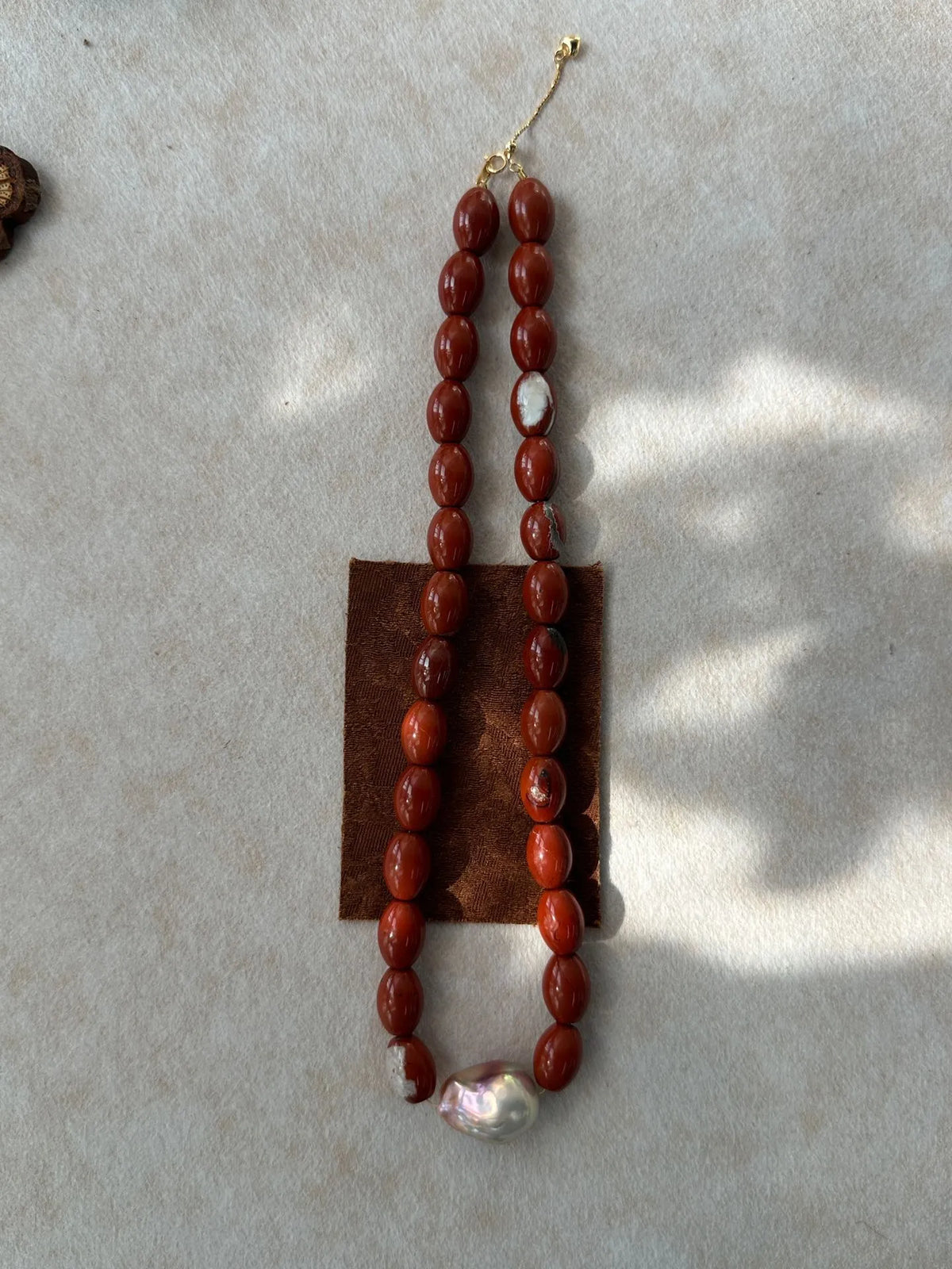 Vertical flatlay of red jasper gemstone beads featuring a luminous baroque pearl.