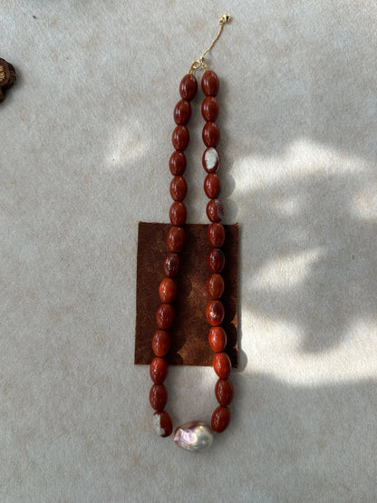 Vertical flatlay of red jasper gemstone beads featuring a luminous baroque pearl.