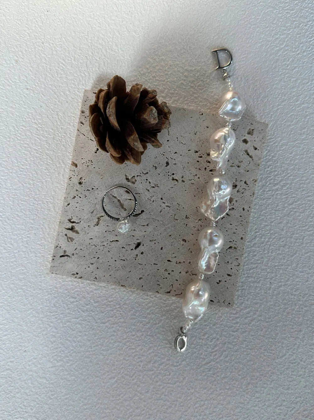 Vertical flatlay of the rice and large baroque pearl strand with a pearl ring on travertine slab.